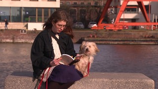 Die Buchautorin Jennifer Wrona sitzt am Wasser mit ihrem Hund und liest ihr eigenes Buch. 