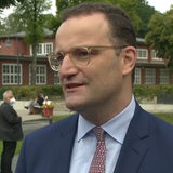 Ein etwa 40 Jahre alter Mann mit kurzen Haaren, Brille, Anzug und Krawatte steht blickt einen Gesprächspartner an.