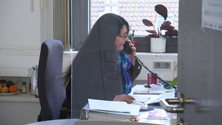Eine Mitarbeiterin des Jobcenters sitzt in ihrem Büro hinter einer Plexiglasscheibe und telefoniert.