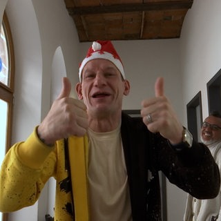 Ein Mann hebt beide Daumen und lächelt in die Kamera.