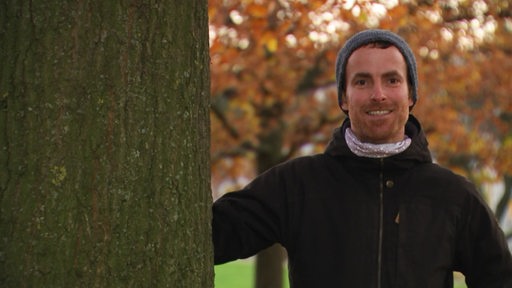Der Umweltwissenschaftler und Projektleiter von Bremen erneuerbar Jonas Daldrup steht neben einen Baum. 