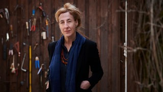 Die Autorin Judith Hermann steht vor einer Bretterwand mit Werkzeug