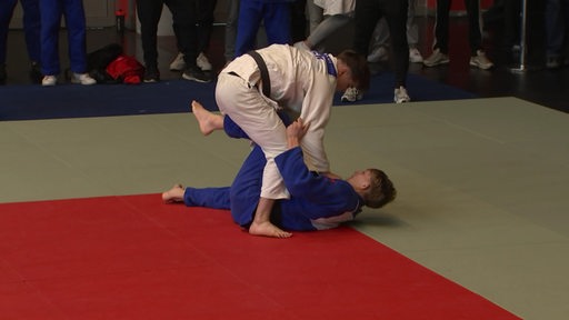 Zwei Männer, die miteinander kämpfen. Beide tragen Judoanzüge.