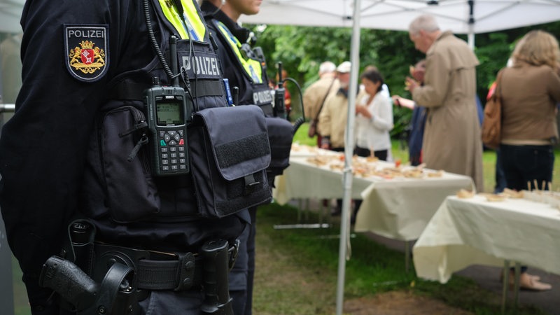 Polizeischutz bei einer Veranstaltung der Jüdischen Gemeinde im Land Bremen. Im Vordergrund sind zwei Polizisten zu sehen und im Hintergrund Menschen, die draußen unter Zelten an langen Tischen essen. 