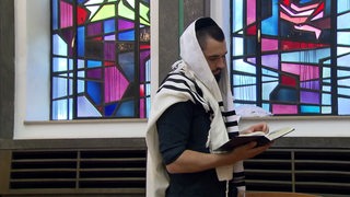 Der jüdische Mann Akiva steht in der Synagoe und liest die Thora. 