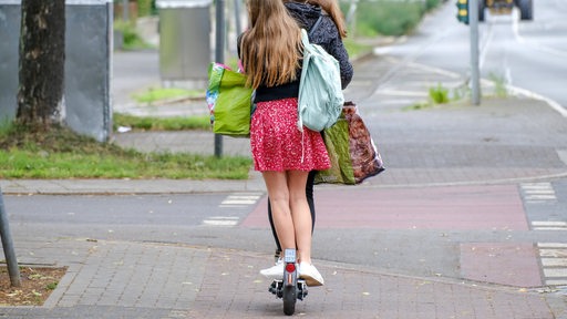 Zwei jugendliche Mädchen fahren zusammen auf einem E-Scooter