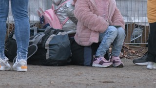 Junge Menschen sitzen auf Gepäck und warten. 