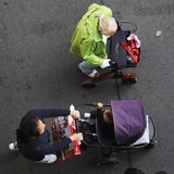 Eine alte Frau mit Rollator geht neben einer Mutter, die einen Kinderbuggy schiebt über die Straße. Als Aufsicht fotografiert