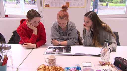 Drei junge Frauen schauen sich ein Buch mit Fotos an.