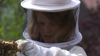Der Jugendliche Jonte Mai in ienem Imkeranzug, der ein Teil eines Bienenhauses in der Hand hält.