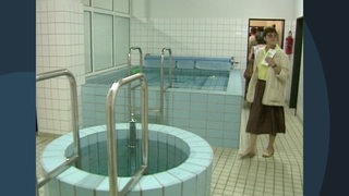 Es ist eine Frau zu sehen, die in einem Raum mit zwei Schwimmbecken steht. Diese Becken befinden sind in der Kabine von Werder Bremens Fußballspieler.