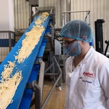 Ein Mitarbeiter steht neben einem Fließband mit Schmelzkäse.