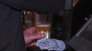 Unter einer Kaffeemaschine steht ein Glas, in welchem ein Latte Macchiato zubereitet wird.