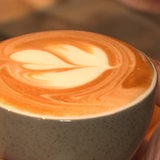 Eine Hand hält eine Tasse Kaffee mit Coffee-Art.