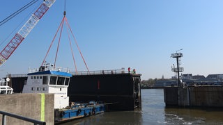 Ein Schiff hebt mit einem Kran einen Teil der Kaiserschleuse an