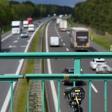 An einem Brückengeländer einer Autobahnbrücke ist eine Kamera angebracht.