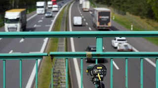 An einem Brückengeländer einer Autobahnbrücke ist eine Kamera angebracht.