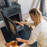Eine Frau legt Holz in ihren Kamin im Wohnzimmer.