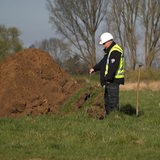 Ein Mann in Warnweste steht neben einem Erdhaufen.