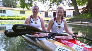 Die Bremer Kanutinnen Hjördis Sommer und Marit Behrens sitzen nebeneinander im Kanu mit den Paddeln in den Händen bei einem Interview.
