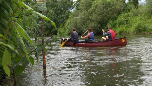 Drei Personen sind in einem Kanu auf einem Fluss unterwegs.