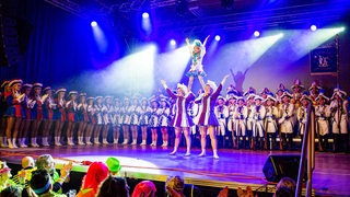 Garde-Tänzerinnen und Tänzer stehen im Kostüm auf der Bühne im Festzelt