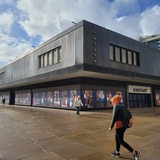Menschen gehen vor einem großen blauen Gebäude entlang.