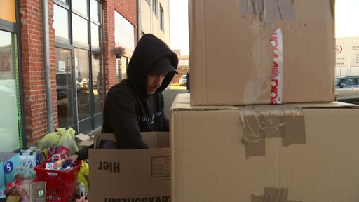 Ein Mann schaut in einen Karton. Im Hintergrund sind Tüten und Säcke zu erkennen.