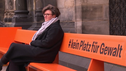 Eine Frau sitzt auf der Bank vor dem Bremer Dom mit der Aufschrift # kein Platz für Gewalt. 