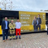 Neben einem Bus mit der Aufschrift "Menschen bewegen ohne Gewalt erfahren" stehen fünf Personen.