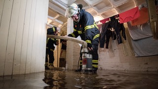 Feuerwehrleute pumpen nach einem Unwetter mit Starkregen Wasser aus dem Keller eines Mehrfamilienhauses ab. 