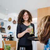 Eine junge Frau serviert einen einen Cocktail in einer Bar. 