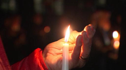 Eine Hand hinter der Flamme einer Kerze.