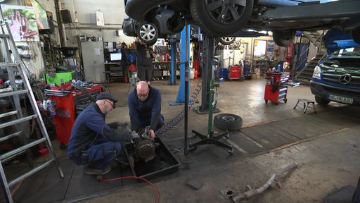 Zwei KFZ-Mechaniker in einer Autowerkstatt am schrauben.