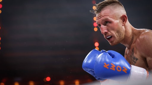 Kickboxer Pascal Schroth in Aktion mit blauen Boxhandschuhen im Ring.