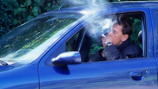 Ein junger Mann raucht im Auto einen Joint.