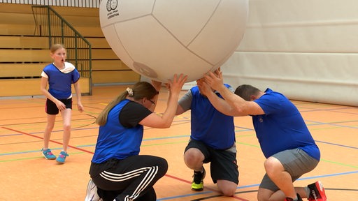 Eine Kin-Ball-Spielerin setzt zum Schlag an, während ihre drei Mitspieler die Aufschlagposition bilden.