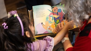 Ein Kind und eine Frau blättern zusammen in einem Bilderbuch.