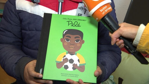 Ein Kind hält ein Buch über den Fußballspieler Pelé in den Händen.