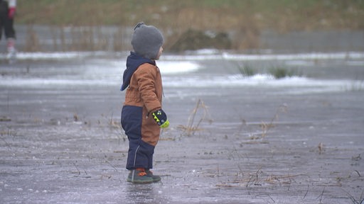 Zu sehen ist ein Kind, welches auf einer gefrorenen eisfläche steht.