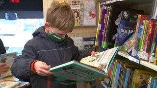 Ein Junge schaut sich im Stadtbibliotheksbus ein Buch an. Neben ihm sind viele bunte Buchrücken in Regalen zu sehen.