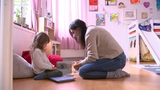 Eine Mutter liest einem Kind in einem Kinderzimmer etwas vor.