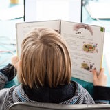 Ein Kind sitzt an einem Tisch und hat ein Schulbuch in der Hand