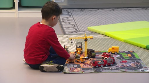 Ein Kind spielt alleine auf einem Teppich mit diversen Fahrzeugen.