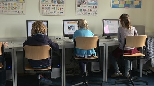 Drei Kinder sitzen an Computern in der Schule.