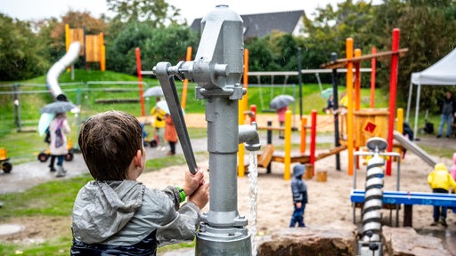Ein Junge spielt auf einem Spielplatz mit einer Wasserpumpe.