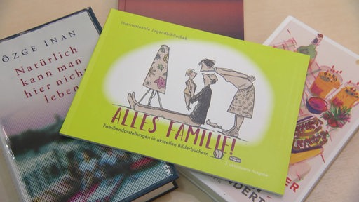 Ein haufen mit unterschiedlichsten Büchern. Das oberste Buch trägt den Titel: "Alles Familie!"
