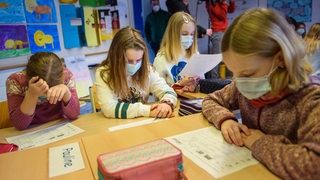 Schülerinnen einer 4. Klasse lesen im Unterricht  mit Maske