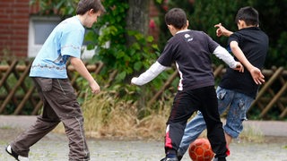 Kinder spielen in einer Einfahrt Fußball
