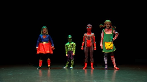 Als Superheldinnen und Superhelden verkleidetet Kinder stehen auf einer Bühne.